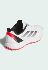 White athletic shoe with black and red accents, featuring a sleek design, perforated detailing, and a textured, rubber outsole for traction.