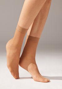 Calcetines de tobillo beige con una textura suave y bandas elásticas en la parte superior. El material transparente revela el tono de piel debajo.