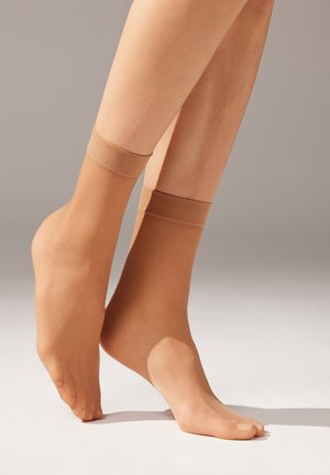 Beiga ankelsockor med en slät textur och elastiska band upptill. Det genomskinliga materialet avslöjar hudtonen under.