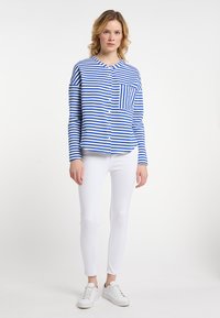 Blauw-wit gestreepte button-up shirt met een ronde hals, enkele borstzak, gecombineerd met witte skinny jeans en witte sneakers.