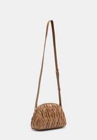 Sac à bandoulière en cuir tan avec une sangle réglable, de forme incurvée, motif matelassé et fermeture éclair, présentant une texture lisse et une silhouette douce.