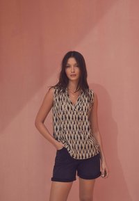 Sleevless beige top med et sort abstrakt mønster, kombineret med mørke oprullede denim shorts. Glat stoftekstur, afslappet pasform, simpel krave.