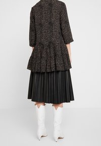 Czarny top w stylu peplum w wzór z trzema ćwierć rękawami, nałożony na plisowaną czarną spódnicę, połączony z białymi kowbojskimi botkami.