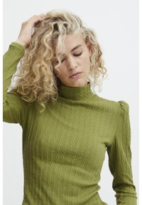 Maglietta lunga verde oliva con texture e collo alto, caratterizzata da motivi a coste e maniche leggermente a sbuffo.