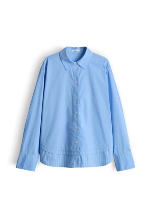 Camicia azzurro chiaro a maniche lunghe con bottoni, colletto, polsini estesi e un pannello a righe leggermente più lungo sull'orlo posteriore.