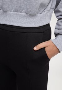 Felpa grigia con polsini a coste abbinata a pantaloni neri con tasca laterale e texture liscia.