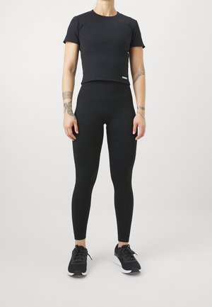 Camiseta corta negra con cuello redondo y mangas cortas, combinada con leggings negros de cintura alta. Zapatillas completan el look.