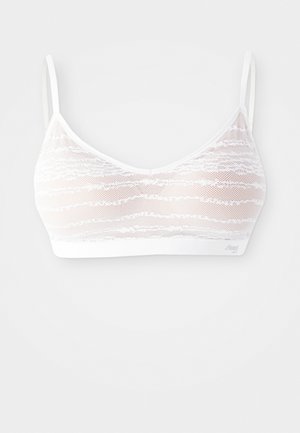 Bela čipkasta braletka z valovitim vzorcem, nastavljivimi naramnicami in mehkimi pasovi. Ima prosojno teksturo z gladkim zaključkom.