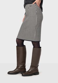 Rutig blyertskjol i svart och vitt, i kombination med knähöga bruna läderstövlar och svarta strumpbyxor.