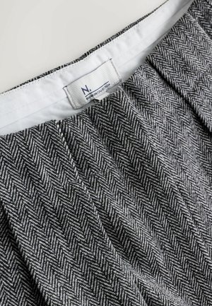 Stoff mit Hahnentrittmuster in Schwarz und Weiß, ausgestattet mit einem Bund mit Herstelleretikett. Glatte Textur, gefaltetes Design.