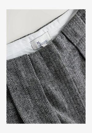 Stoff mit Hahnentrittmuster in Schwarz und Weiß, ausgestattet mit einem Bund mit Herstelleretikett. Glatte Textur, gefaltetes Design.