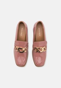 Mocassins en cuir verni rose avec une semelle plate, une large bride ornée d'un détail en chaîne dorée et noire, et un design à bout arrondi.