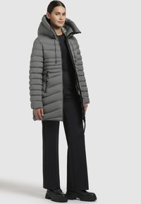 Giacca puffer grigia con colletto alto, tasche con zip e texture a coste. Abbinata a pantaloni neri a gamba larga e stivali neri chunky.
