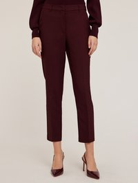 Pantalons bordeaux ajustés, offrant une coupe slim, avec un devant plat, des poches latérales et une longueur cheville, accompagnés de chaussures à talons hauts brillantes.