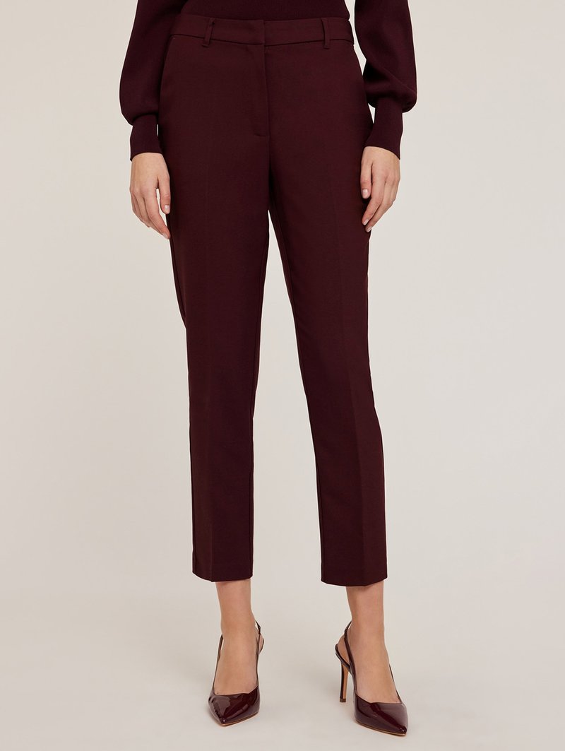 Pantalons bordeaux ajustés, offrant une coupe slim, avec un devant plat, des poches latérales et une longueur cheville, accompagnés de chaussures à talons hauts brillantes.