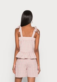Top peplum em padrão vichy rosa e branco com alças ajustáveis, combinado com calções a condizer. O tecido é texturizado, leve e descontraído.