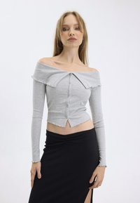 Sivi rebrasti krojeni top s otpadnim rubom i detaljem gumba, kombiniran s crnom uskom suknjom s bočnim izrezom.