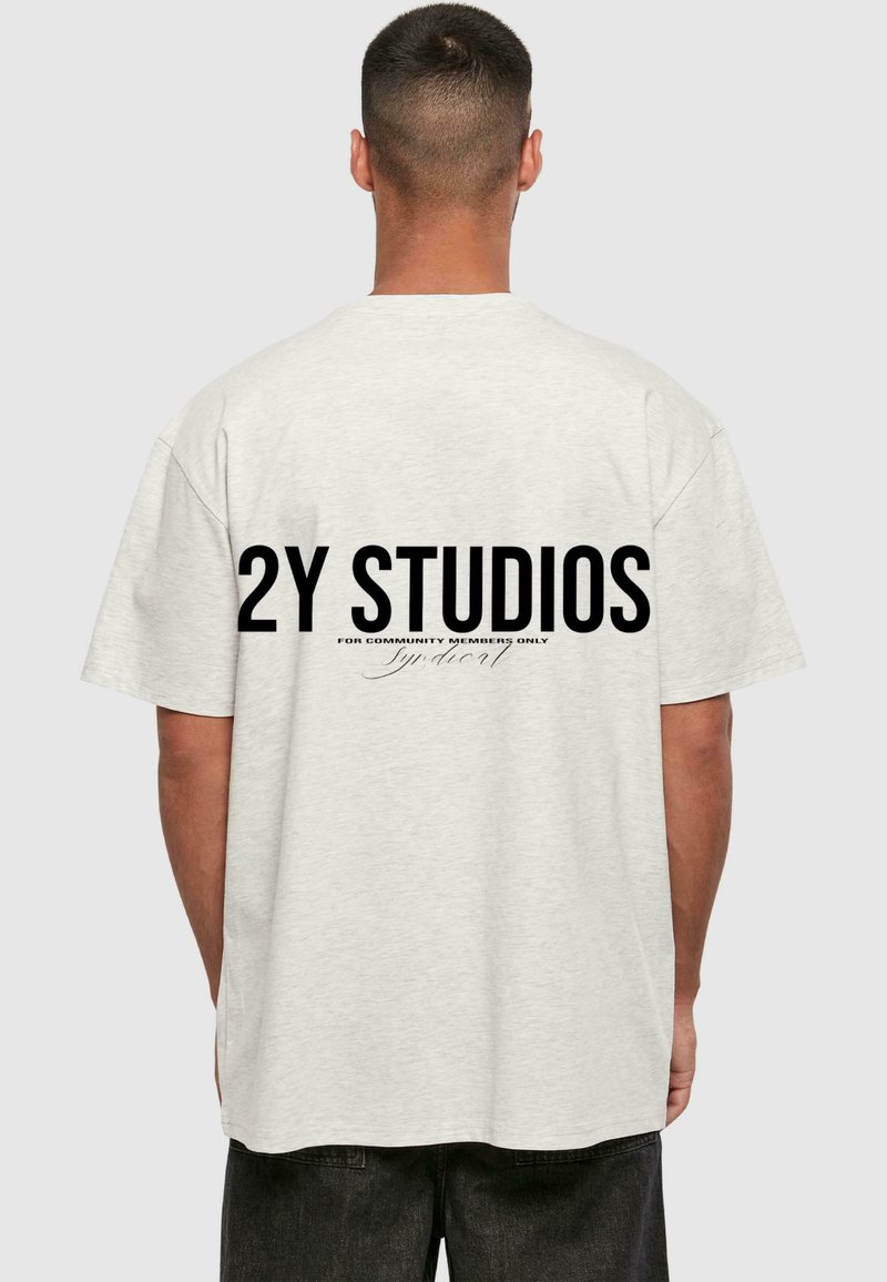 Lys grå, overdimensjonert T-skjorte med korte ermer. Har store svarte bokstaver på baksiden: "2Y STUDIOS" og mindre tekst under.