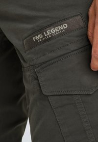 Pantalon cargo vert foncé avec une poche dotée d'un patch texturé portant l'inscription "PME LEGEND AMERICAN CLASSIC" et des détails de couture visibles.