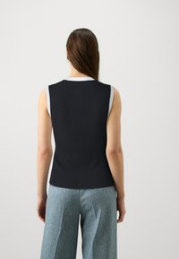 Μαύρο ριγέ αμάνικο τοπ με λευκή στρογγυλή λαιμόκοψη, συνδυασμένο με ανοιχτό μπλε φαρδιά παντελόνια, προ εμφανίζεται από πίσω.