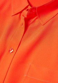 Jasnopomarańczowa koszula z kołnierzykiem, wykonana z miękkiego materiału, z listwą guzikową, jedną kieszenią na piersi i gładką, teksturowaną powierzchnią.