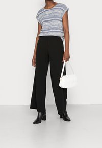 Top corto de rayas grises con mangas cortas combinado con pantalones negros de pierna ancha, botas de tobillo negras con tacón y un bolso acolchado blanco.