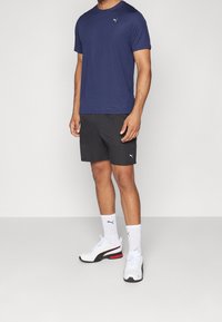 Námornícké sportovní tričko s kulatým výstřihem, spárované s černými šortkami. Bílé ponožky a boty s červenými akcenty dokončují outfit.