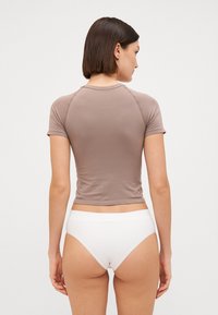 Short-sleeve, fitted top in taupe, made of stretchy fabric. Pair of white, seamless high-waisted briefs, displayed from the back.