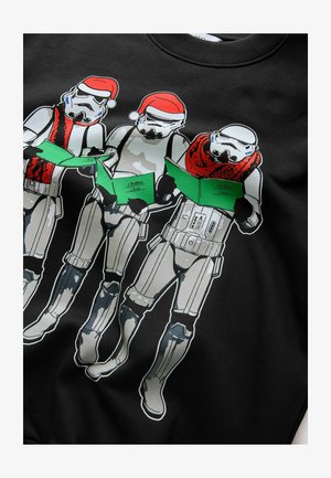 Melnā sporta krekls ar trim stormtrooperiem Ziemassvētku cepurēs, kuri tur zaļas Ziemassvētku kartiņas. Dizains ir grafisks un krāsains ar detaļām.