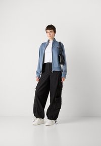 Blue faux leather jacket with ribbed cuffs, white cropped top, black cargo pants with pockets, and white sneakers. Small black handbag.