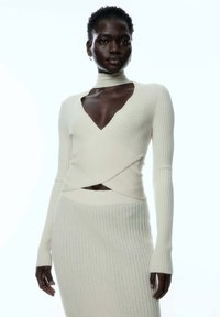 Weißes, geripptes Strickkleid mit tiefem V-Ausschnitt, langen Ärmeln und einem offenen Taillen-Detail. Weicher Stoff mit einer figurbetonten Silhouette.