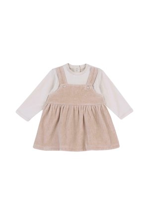 Robe salopette en velours côtelé beige portée sur un body blanc à manches longues pour bébé avec des boutons-pression au niveau du col.