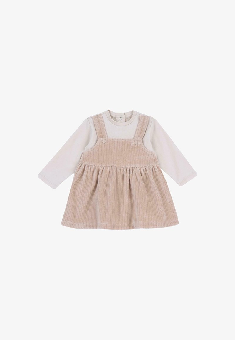 Robe salopette en velours côtelé beige portée sur un body blanc à manches longues pour bébé avec des boutons-pression au niveau du col.