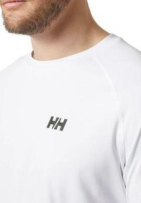 Camiseta blanca de mangas cortas con cuello redondo y un pequeño logo negro "HH" en el pecho. Hecha de un material suave y ligero.