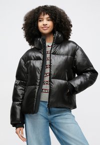 Μαύρο φουσκωτό μπουφάν με γυαλιστερό φινίρισμα, ψηλό γιακά, πλήρες φερμουάρ και λογότυπο στον γιακά. Διαθέτει διπλές πλαϊνές τσέπες και κουτιώδες σχήμα.