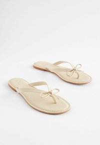 Beige flip-flopit, joissa on ohut hihna ja edessä kaunis nauhakoriste. Suora pinta, litteä pohja ja minimaalinen ompelu.