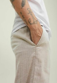 Jasnobeżowe spodnie w jodełkę z boczną kieszenią, zestawione z białym t-shirtem. Gładka tekstura, luźny krój i widoczne detale przeszyć.