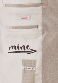 Das Innenfutter der schlanken Jacke besteht aus einem leichten Stoff mit roter Naht. Auffällige Aufdrucke sind "mine" und "DO YOU AGREE?" auf hellbraunen Etiketten.