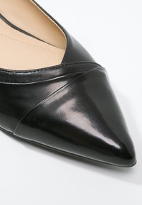 Mocassin noir à bout pointu avec une finition brillante en cuir verni et une couture cousue à la base. Texture lisse et design élégant.