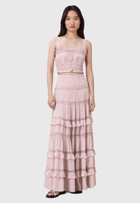 Rosa to-delt outfit med en cropped top med smocket bodice og en lang lagdelt nederdel med volangdetaljer. Glat stof, delikat syning.