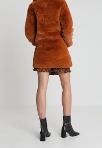 Płaszcz z futerka sztucznego w kolorze spalonym pomarańczowym, do kolan, z zaokrąglonym kołnierzem, z długimi rękawami. Noszony na wzorzystej spódnicy, zestawiony z czarnymi kozakami na obcasie.