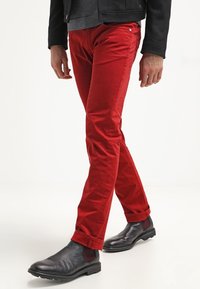 Cino in cotone rosso con vestibilità slim, caratterizzati da orli arrotolati e dettagli di cucitura discreti, abbinati a stivali Chelsea in pelle nera.