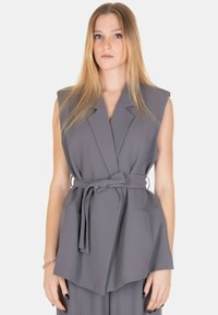 Gilet grigio senza maniche con vita con cintura, rever a lancia e due tasche frontali, realizzato in tessuto liscio con una sottile trama.