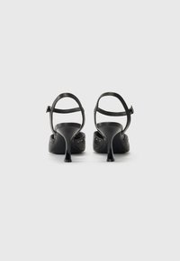 Zwarte hoge hakken sandalen met een gladde leren afwerking, verstelbare enkelriemen en decoratieve zilveren studs aan de zijkant.