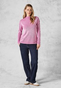 Rosa ribbad tröja med hög krage, kombinerad med mörkblå jeans och vita skor. Tröjan har en åtsittande design och strukturerad tyg.