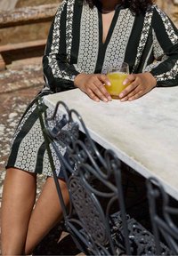 Mustat ja valkoiset kuviot, pitkät hihat, V-pääntie ja kukkakuviot, yhdistettynä lasilliseen keltaista juomaa marmorpöydällä.