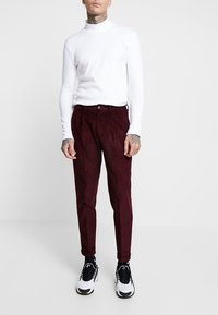 Burgunderfärgade kordbyxor med slim fit, i kombination med en figurnära vit polotröja och svartvita sneakers, som ger en ren och modern stil.