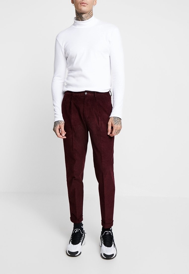 Burgunderfärgade kordbyxor med slim fit, i kombination med en figurnära vit polotröja och svartvita sneakers, som ger en ren och modern stil.