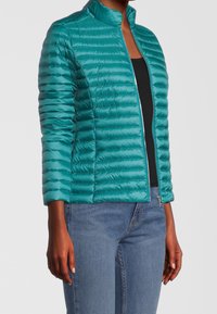 Tyrkysová nadýchaná bunda s stojatým límcem, zapínáním na zip a horizontálním prošíváním. Měkká textura, lehká látka a přiléhavý střih.