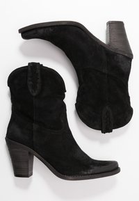 Botas de tobillo de ante negro con tacón apilado, punta afilada y costuras decorativas en la parte superior. Cuenta con una lengüeta en la parte posterior.